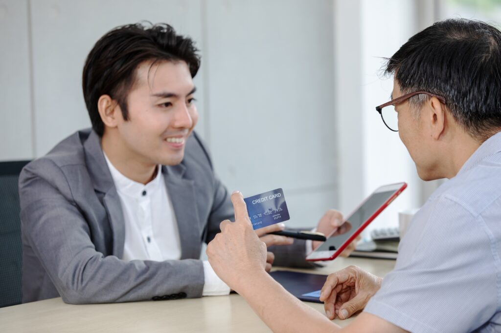 An older man holds a credit card while speaking with a young financial advisor.